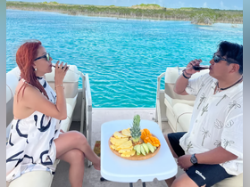A couple enjoys cocktails and a fresh fruit platter on a boat, surrounded by stunning turquoise waters — a perfect setting for relaxation and celebration.