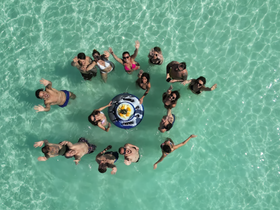 A lively group of friends celebrates in the crystal-clear waters, enjoying a fun-filled day with drinks and laughter — perfect for unforgettable summer memories.