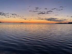 A stunning sunset over calm waters, with silhouettes of distant islands creating a picturesque scene — perfect for capturing the beauty of nature.