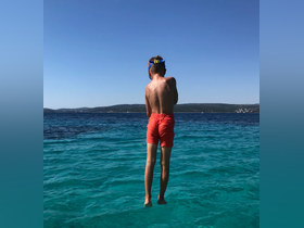 A child prepares to jump into the crystal-clear waters, capturing the essence of summer fun and adventure on a boating trip.