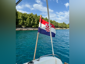 A close-up view of the Croatian flag waving on a boat, set against a backdrop of lush greenery and clear turquoise waters, showcasing the beauty of boating in Croatia.