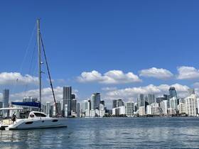 A stunning view of a catamaran anchored in the waters of Miami, with a backdrop of the city's impressive skyline and clear blue skies.