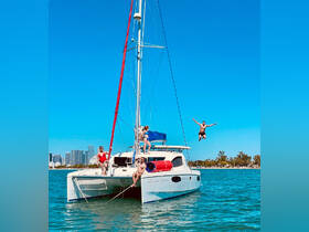 A lively group enjoys a fun day on a catamaran, with one person jumping into the water while others relax on deck — a perfect moment of summer adventure.