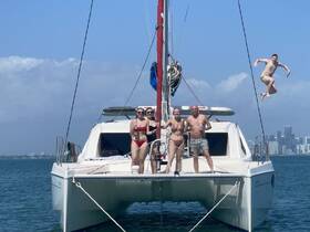 A fun group of friends poses on a catamaran, with one member leaping into the water — a perfect snapshot of summer adventures and celebrations on the water.