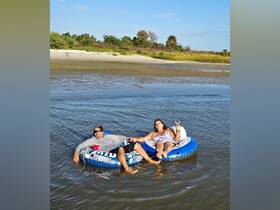 A couple enjoys a relaxing day floating on inflatable tubes in shallow water, capturing the essence of summer fun at the beach.
