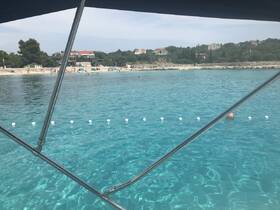 A picturesque view from a boat showcasing a beautiful beach with people enjoying the sun and clear turquoise waters — perfect for a relaxing day on the water.