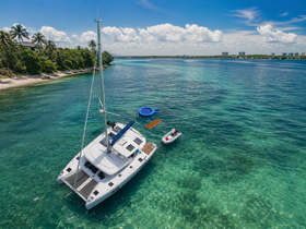 A stunning aerial view of a catamaran anchored in crystal-clear waters, surrounded by lush greenery and a serene beach — perfect for a relaxing day on the water.