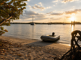 A serene sunset view of a small boat docked on the sandy shore, with larger vessels anchored in the background, creating a picturesque coastal scene.