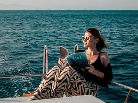 A woman enjoys a moment of relaxation on a boat, reading a magazine while surrounded by the beautiful ocean — a perfect escape for sun-seekers and book lovers.