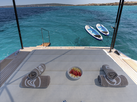 A relaxing setup on a boat deck featuring towels and a bowl of fresh fruit, with paddleboards ready for use in the stunning turquoise waters.
