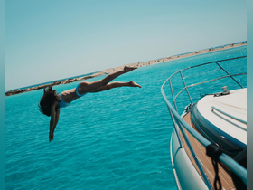 A person joyfully leaps off the side of a boat into the stunning turquoise waters, capturing the essence of summer fun and adventure on the water.