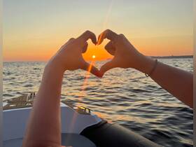 A hand forms a heart shape against a stunning sunset over the water, capturing a romantic moment aboard a boat — perfect for sunset cruises.