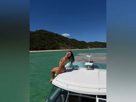 A woman enjoys the sun on the deck of a boat, showcasing a perfect day of fun and relaxation on the water, with a beautiful beach backdrop.