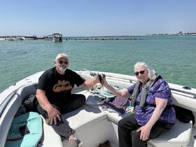 A cheerful couple enjoys a fishing moment on their boat, surrounded by beautiful turquoise waters — a perfect day for relaxation and adventure.