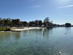 A scenic view of a calm waterway with a sandy beach and palm trees, showcasing a tranquil outdoor environment.