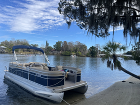 A picturesque view of a pontoon boat docked by the shore, surrounded by serene waters and lush greenery, perfect for a relaxing day on the water.