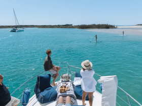A group enjoys a sunny day on a yacht, watching paddleboarders glide across the turquoise waters — a perfect scene for relaxation and adventure.