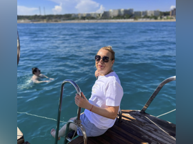 A woman enjoys a sunny day on a boat while another person swims nearby, capturing the essence of fun and relaxation on the water.