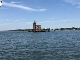 A picturesque view of a historic lighthouse standing on a rocky outcrop, surrounded by calm waters and a clear blue sky — a perfect representation of coastal beauty.