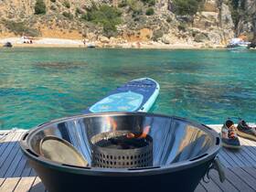 A stylish grill setup on a boat deck, perfect for barbecuing while enjoying the stunning turquoise waters and scenic beach backdrop.