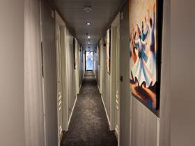 A well-lit hallway inside a boat, featuring artistic paintings on the walls, showcasing the elegant design of the cabin area.