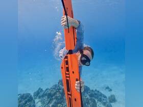 A snorkeler dives underwater with an orange buoy, exploring vibrant marine life in crystal-clear waters — an exhilarating experience for adventure seekers.