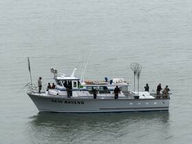 A group of anglers aboard the 'New Rayann' enjoy a fishing trip on calm waters, showcasing the camaraderie and excitement of a day on the sea.
