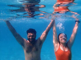 A joyful couple enjoys a fun underwater moment, showcasing their excitement while swimming in crystal-clear waters — perfect for memorable aquatic adventures.