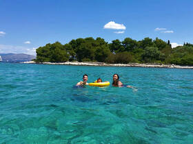 A joyful family enjoys swimming in the crystal-clear waters near a lush island, creating unforgettable memories under the sun.