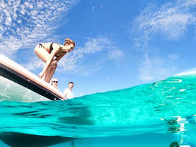 A group of friends enjoys a fun moment as one prepares to jump into the crystal-clear waters from the boat, capturing the essence of adventure on the water.