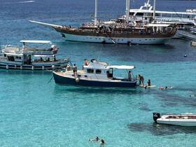 A lively scene featuring a group enjoying the clear turquoise waters, with several boats anchored nearby, perfect for a day of fun and relaxation on the water.