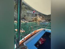 A view of the interior of a boat, showcasing the helm and seating area, with a picturesque backdrop of rocky cliffs and clear turquoise waters.