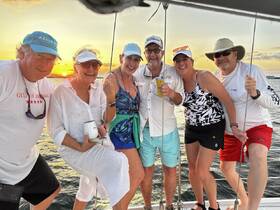 A cheerful group of friends enjoys a sunset celebration aboard a boat, capturing the perfect moment with drinks in hand against a stunning backdrop.