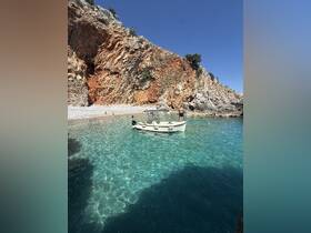 A picturesque scene featuring a small boat anchored near a stunning rocky coastline, with people enjoying the clear waters — perfect for a day of swimming and exploration.