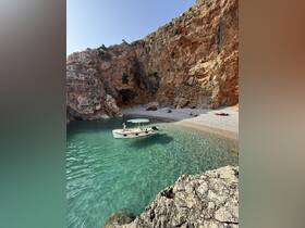 A picturesque scene of a boat anchored near a secluded beach, where guests enjoy the clear waters and stunning rocky backdrop — perfect for a day of relaxation and adventure.