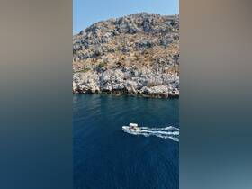 An aerial view captures a boat cruising along a stunning rocky coastline, showcasing the beauty of the open water and the surrounding landscape.