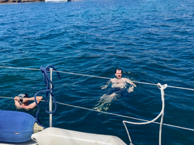 Two individuals enjoy a refreshing swim in the clear waters while a sailboat is anchored nearby, capturing the essence of a perfect day on the water.