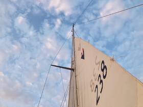 A close-up view of a sailboat's mast and sail against a backdrop of beautiful clouds, showcasing the elegance of sailing.