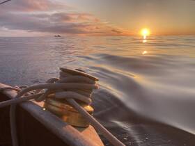 A serene sunset view from a boat, showcasing the calm waters and a rope cleat, perfect for capturing the tranquility of a day on the water.