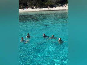 A group of friends enjoys a refreshing swim in crystal-clear waters, with a beautiful beach backdrop — perfect for summer adventures and beach outings.