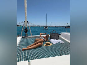 A woman relaxes on the deck of a catamaran, soaking up the sun against a backdrop of stunning turquoise waters — the perfect summer getaway.