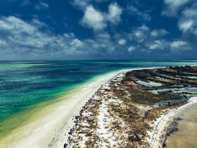A stunning aerial view of a pristine coastline with turquoise waters and sandy beaches, showcasing the natural beauty of the area — perfect for eco tours and scenic boat trips.