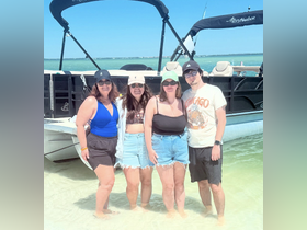 A cheerful group of friends enjoys a sunny day at the beach, standing in shallow water next to their pontoon boat — perfect for summer adventures and memorable outings.