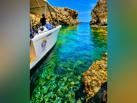A sleek boat navigates through crystal-clear waters surrounded by rocky cliffs, showcasing a perfect day for exploration and adventure.