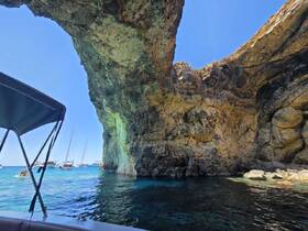 A stunning view of a rocky coastline with multiple boats anchored nearby, showcasing the beauty of the area — perfect for exploring hidden caves and enjoying the crystal-clear waters.