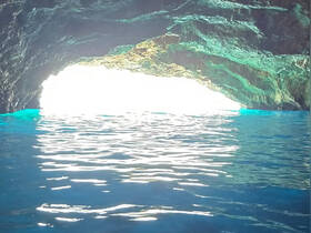 A stunning view of a cave entrance reflecting light over tranquil blue waters, showcasing the natural beauty of coastal landscapes.