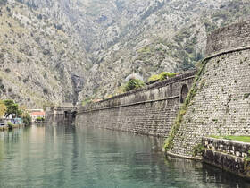 A scenic view of a waterway surrounded by steep mountains and historic stone walls, showcasing the natural beauty and architecture of the area.