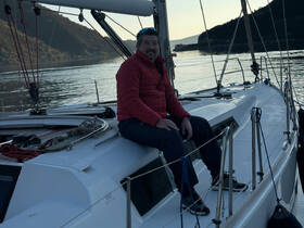 A man relaxes on the deck of a sailboat, enjoying the serene waters and picturesque landscape — perfect for sailing enthusiasts and sunset cruises.