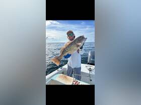 A proud angler holds up a large grouper caught while fishing on the open ocean — a perfect moment for fishing enthusiasts.