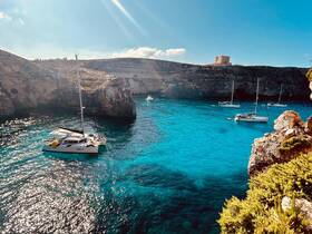 A stunning view of a catamaran sailing in crystal-clear turquoise waters, surrounded by dramatic cliffs — an ideal setting for a relaxing day on the water.